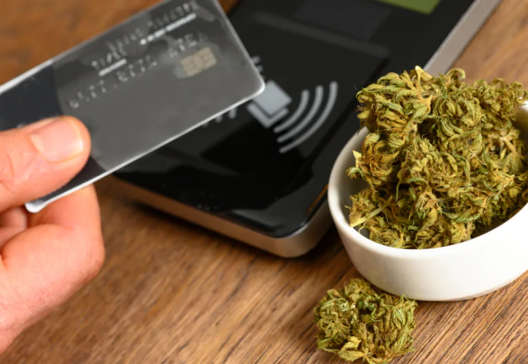 Person tapping their credit card on a payment gateway with marijuana to the side