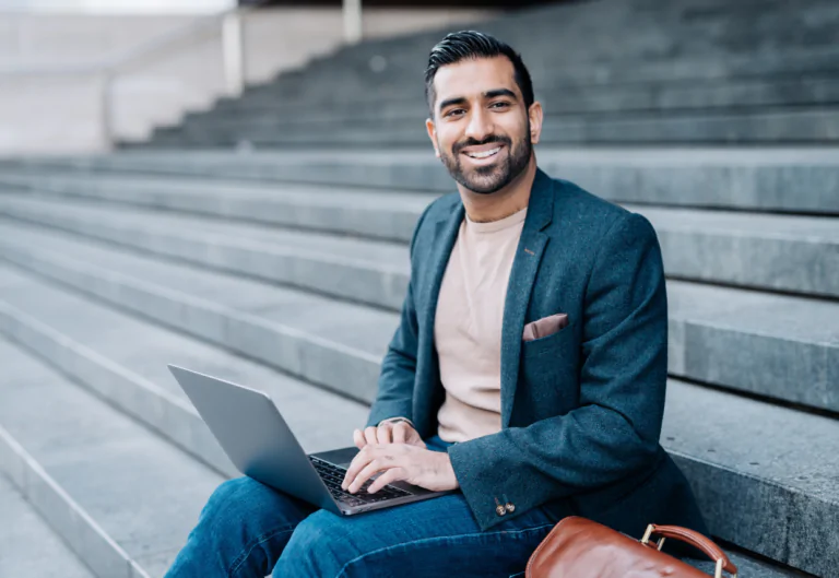 Man sitting on steps smiling as he types on a laptop