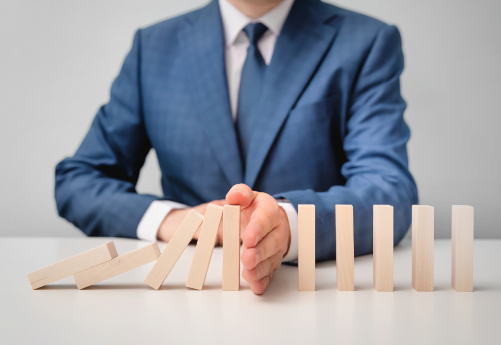 Man in a suit stopping a domino effect of wooden blocks